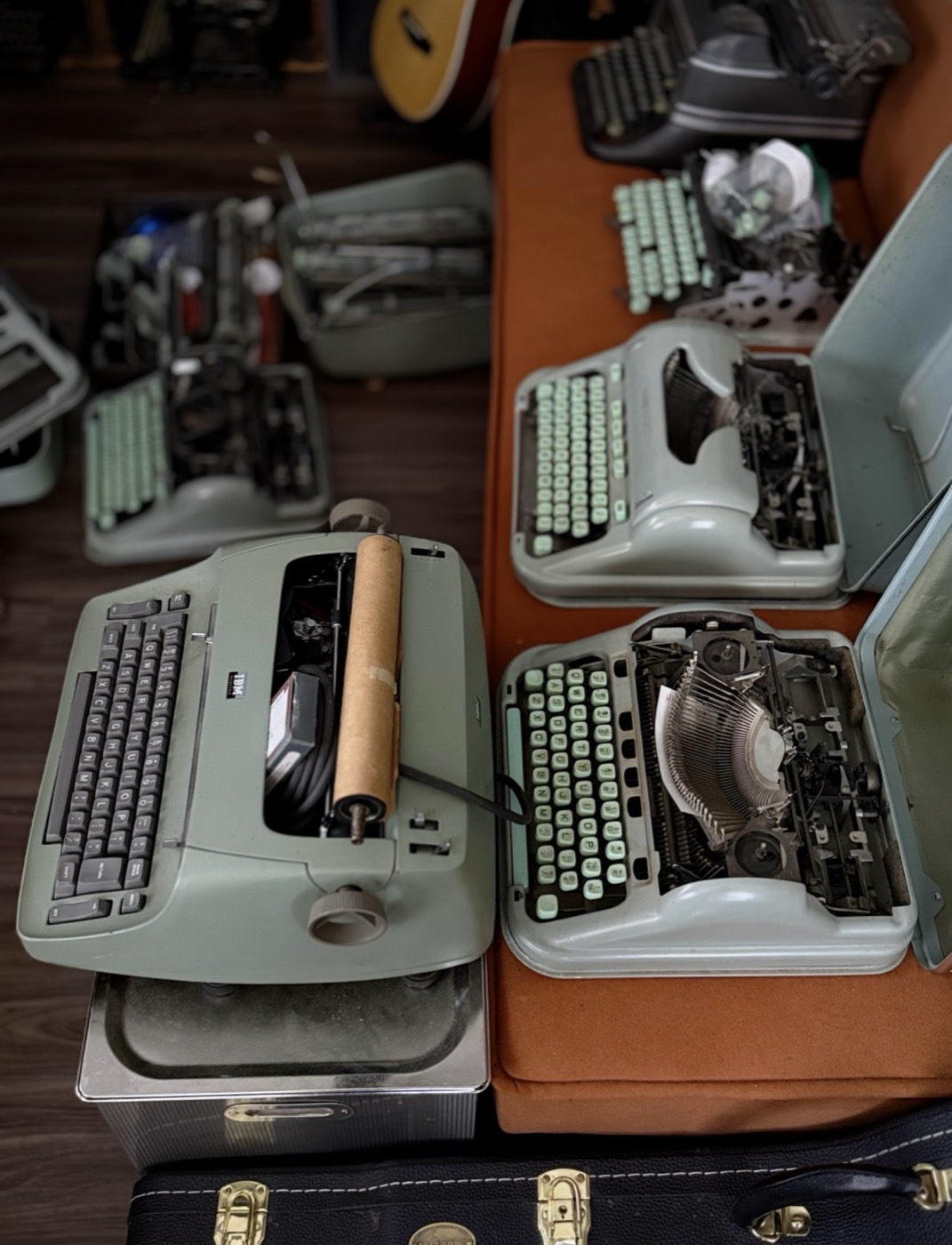 Seafoam-green Hermes typewriters opened up mid-repair on a workbench, seen from above, with an IBM Selectric alongside.