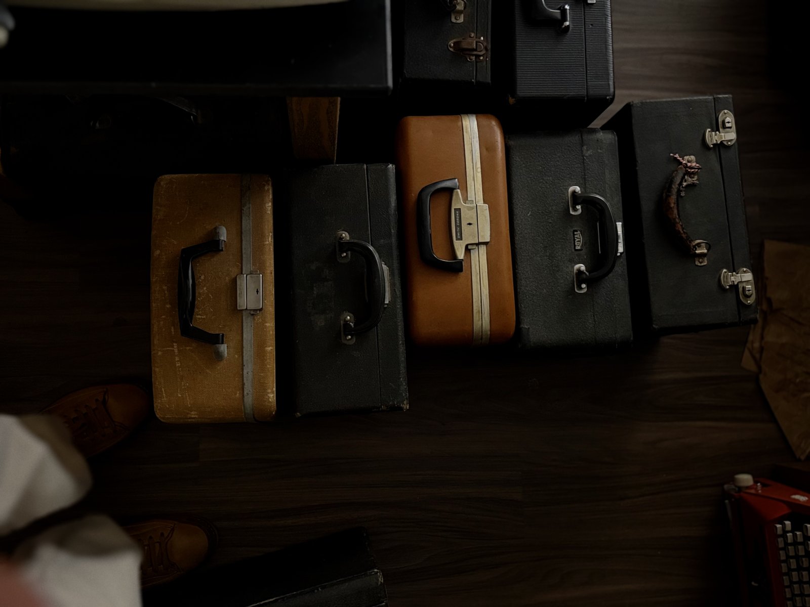 A row of vintage suitcases and typewriter cases laid out on the floor, seen from above, in a mix of gold, black, and tan leather.