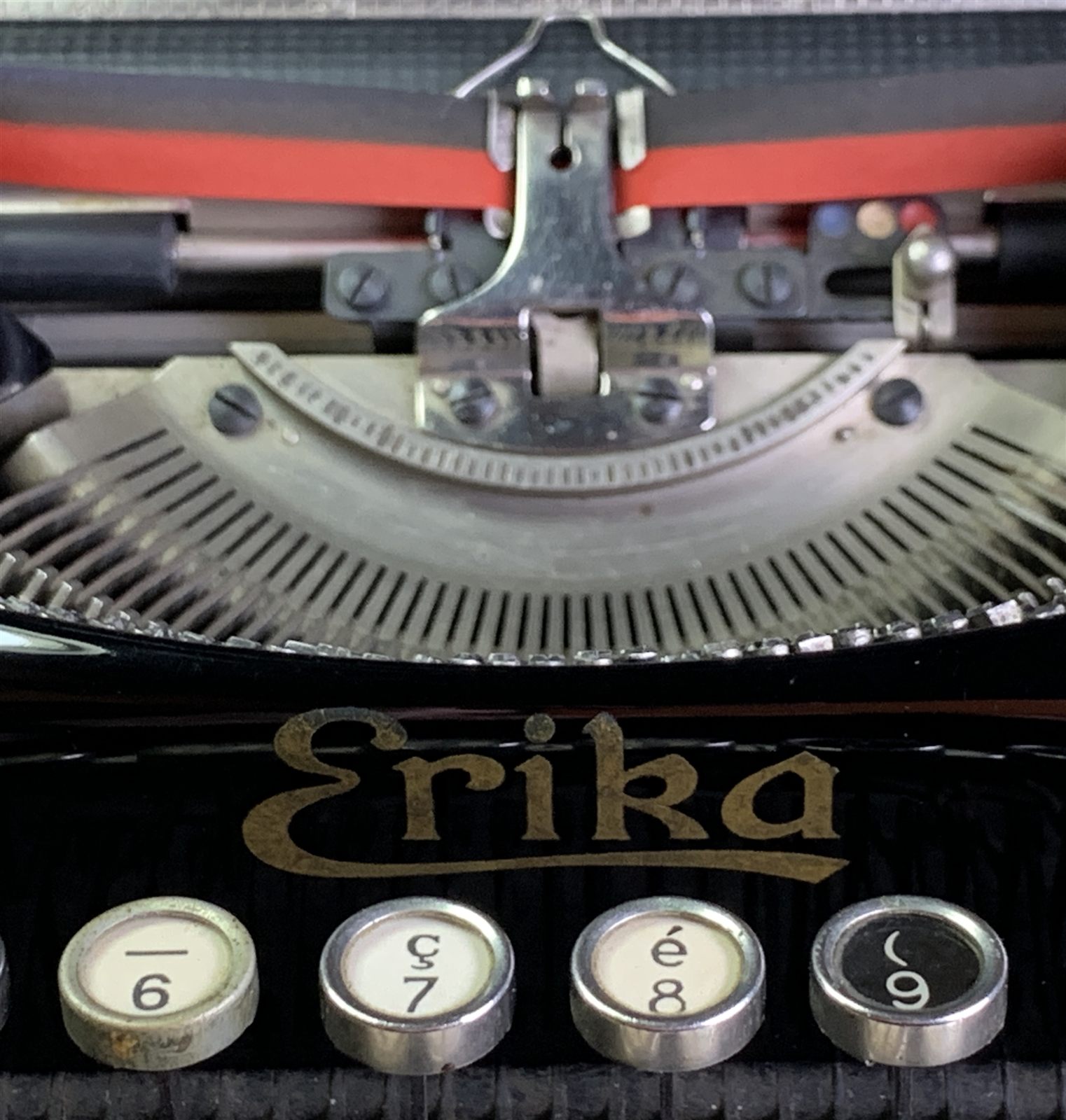 Macro shot of an Erika typewriter's type segment and ribbon, with the gold Erika nameplate and number keys in focus.