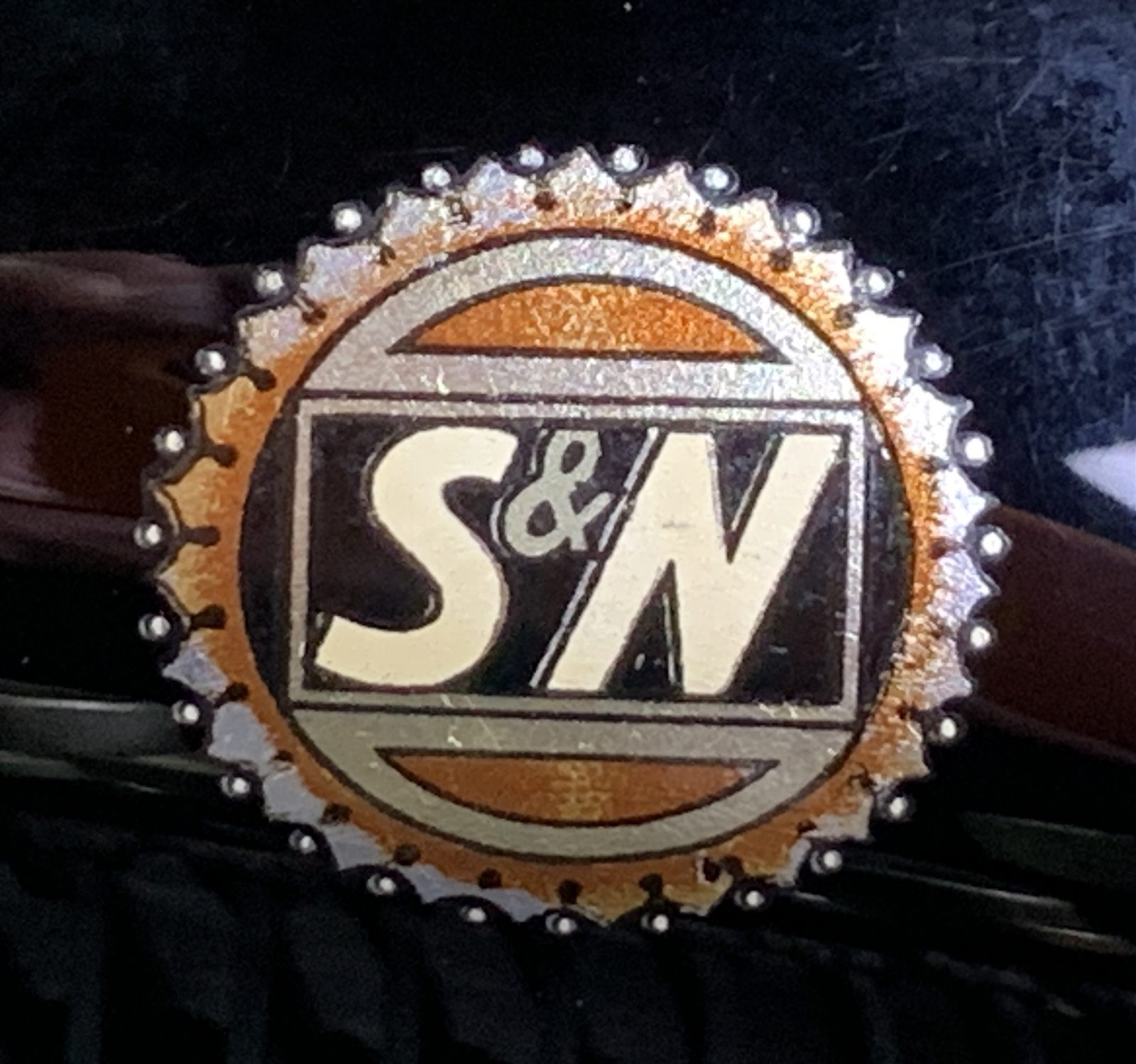 Close-up of a round enamel S&N badge mounted on a typewriter case strap.