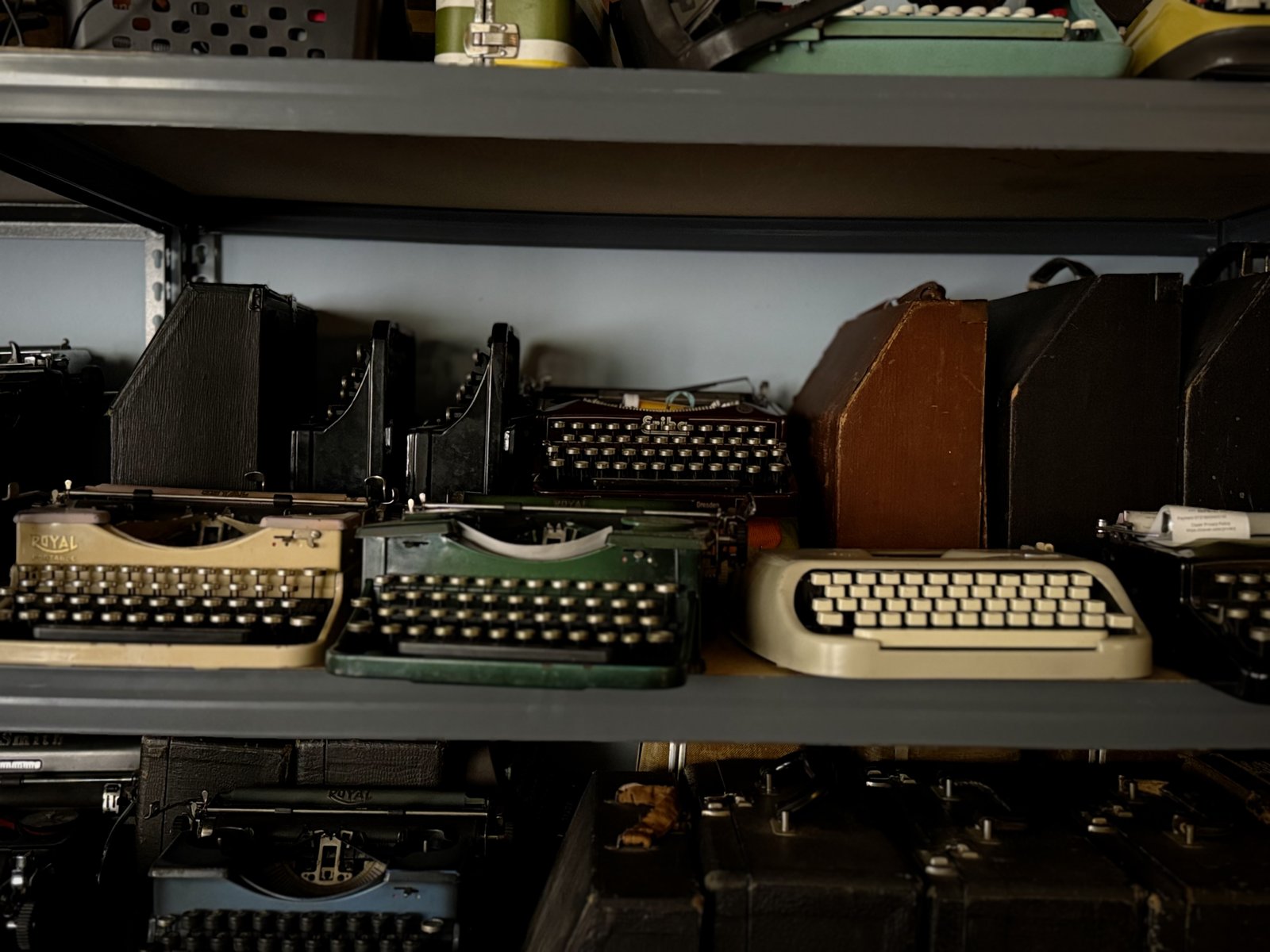 A shelf of typewriters loosely sorted by color, seafoam to rust to cream.