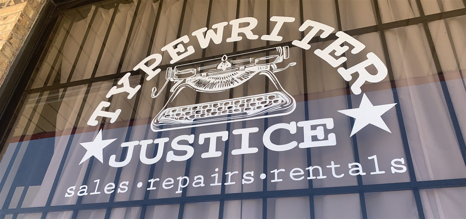 The shop's front window, lettered with the Typewriter Justice logo and sales, repairs, rentals.