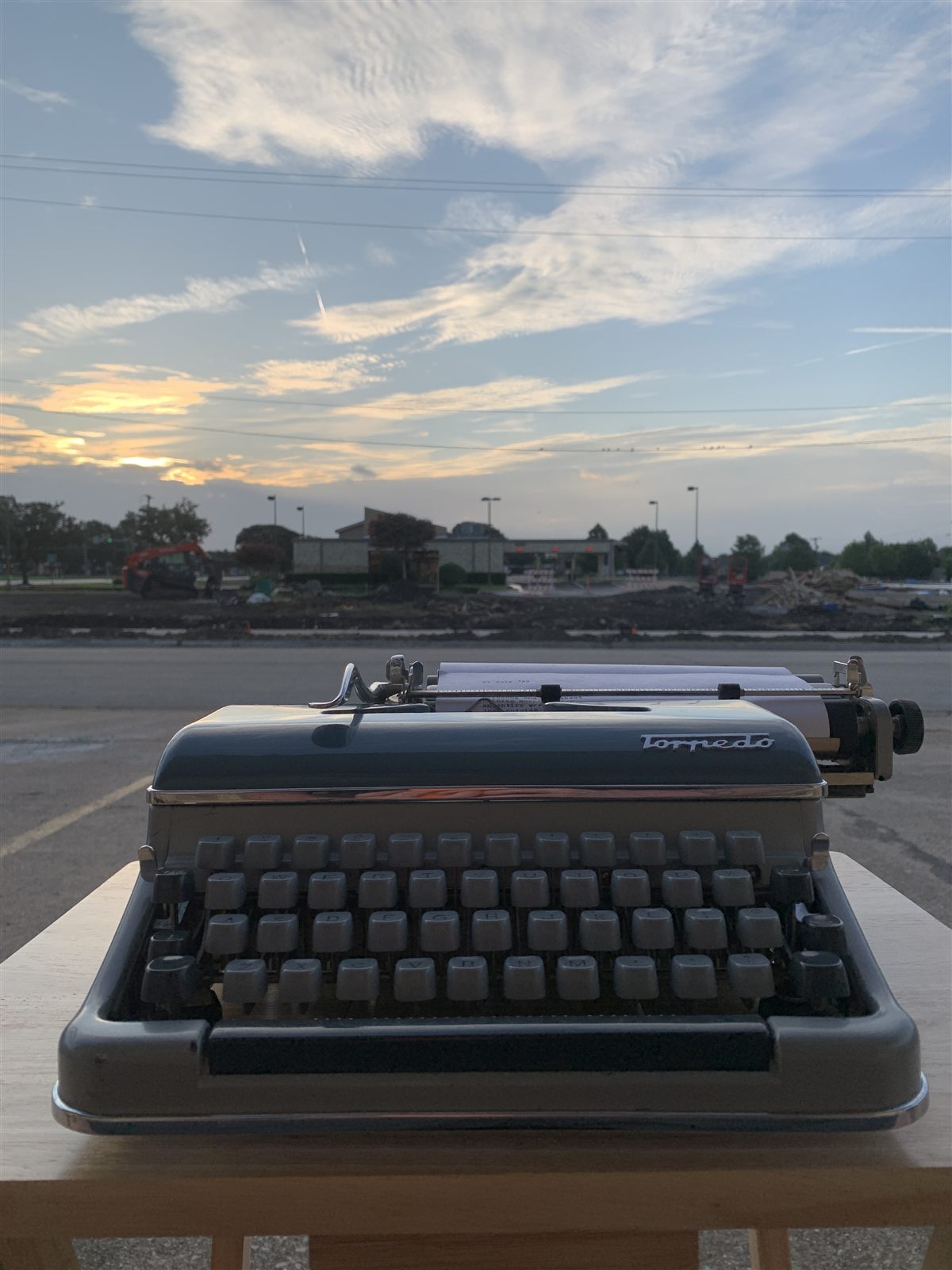 A typewriter set on an outdoor table at sunrise, with colorful clouds filling the sky behind it.