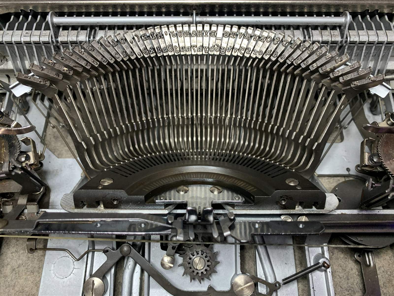 An overhead view of a typewriter's typebars arced open beneath the segment, gears and screws visible at the edges.
