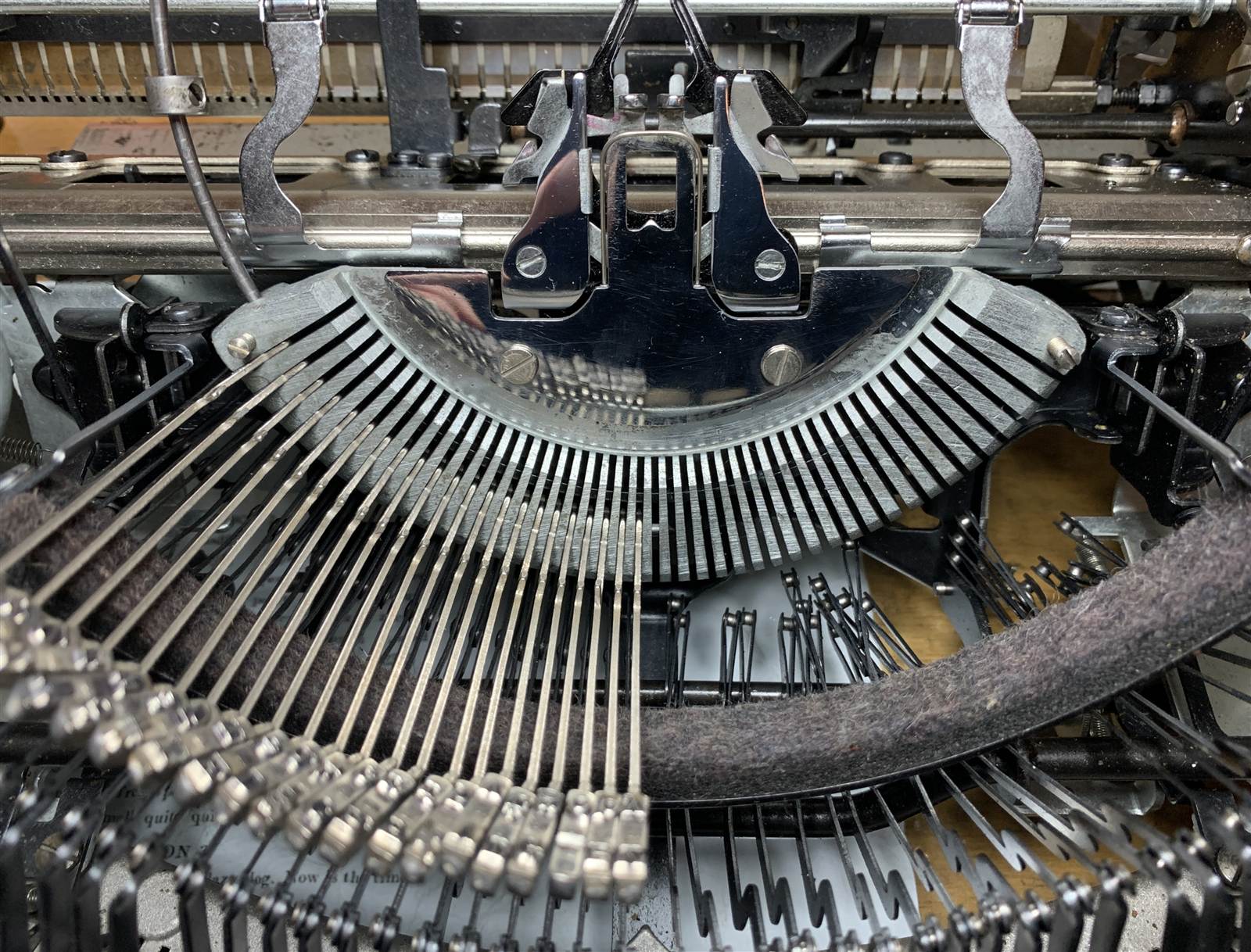 Close-up of a typewriter's typebars fanned out beneath the segment, a felt sheet and papers visible behind.