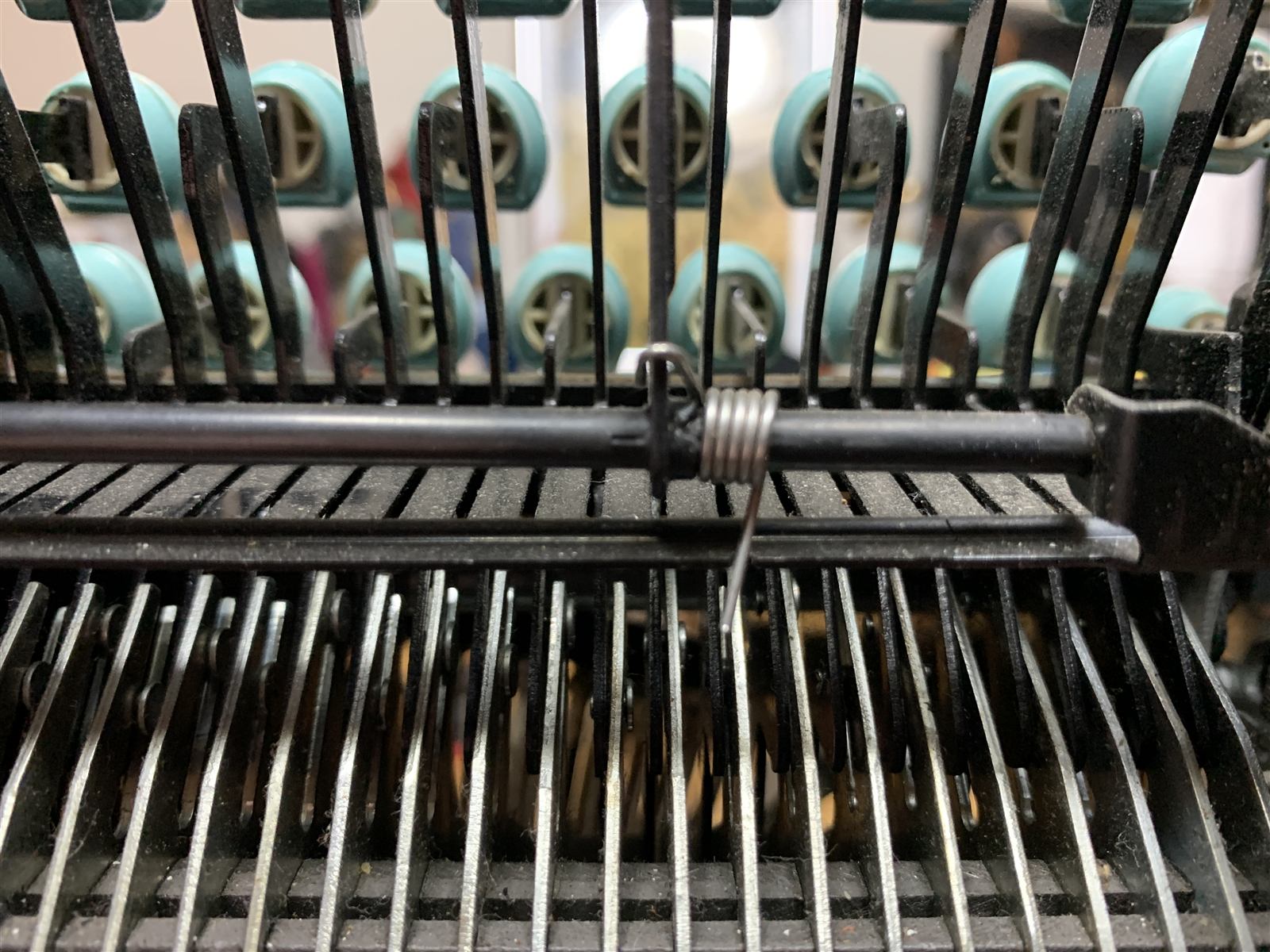 Macro shot of typebars with a wire spring threaded between them, seafoam ribbon spools blurred in the background.