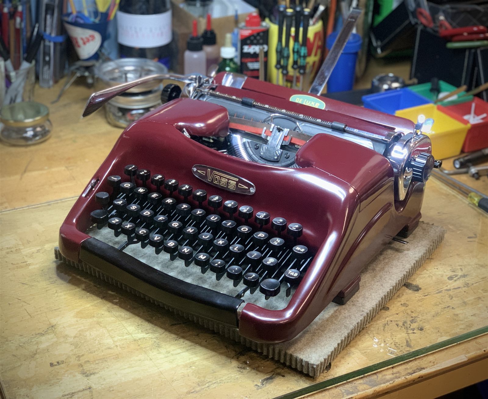 A glossy maroon Voss portable typewriter posed on a padded case on the workbench.