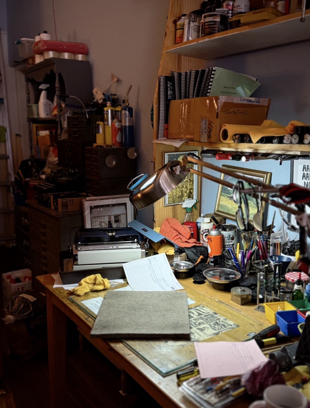 The repair bench: felt sheet, oils, brushes, small tools, ribbon tins, and paperwork under an articulated lamp.